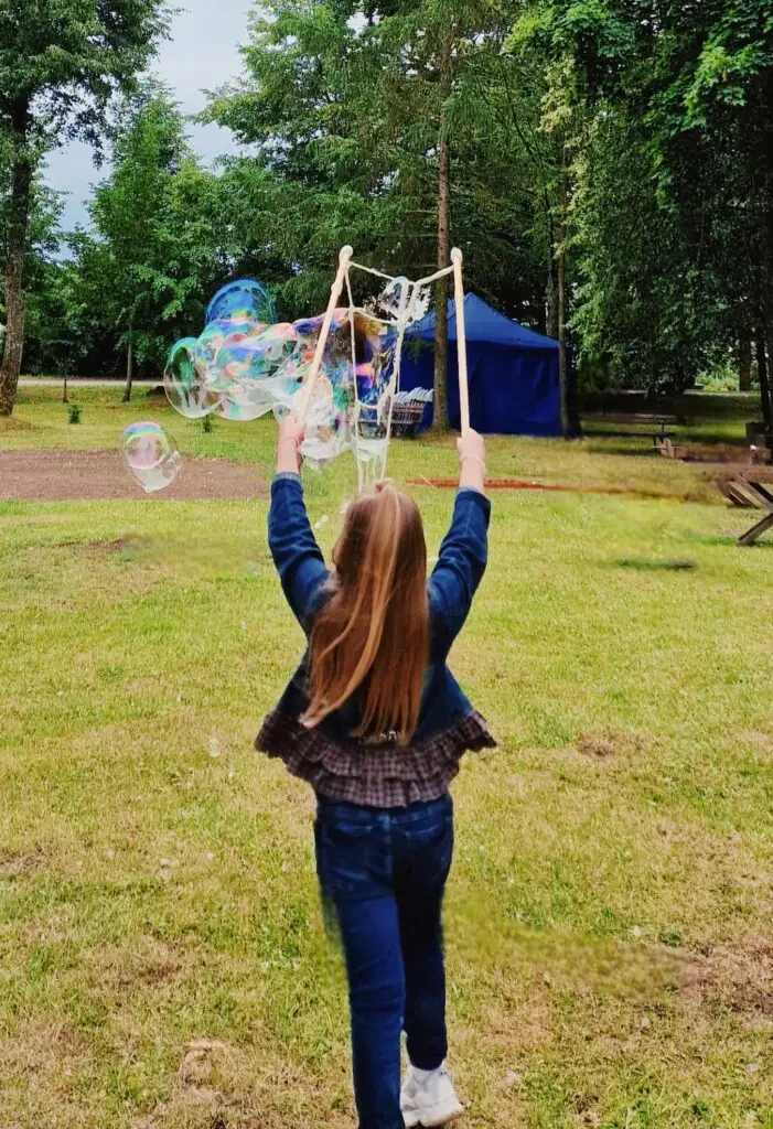 Vaikai žaidžia su dideliais muilo burbulais naudodami medines burbulų lazdeles lauko šventėje