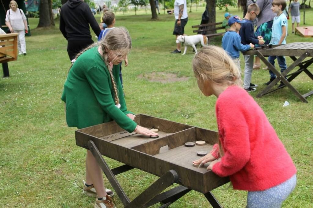 Medinis lauko žaidimas „Skraidančios šaškės“ su išdėliotomis medinėmis šaškėmis ant stalo. Lauko žaidimų gaminimas Lietuvoje, Medžio karma
