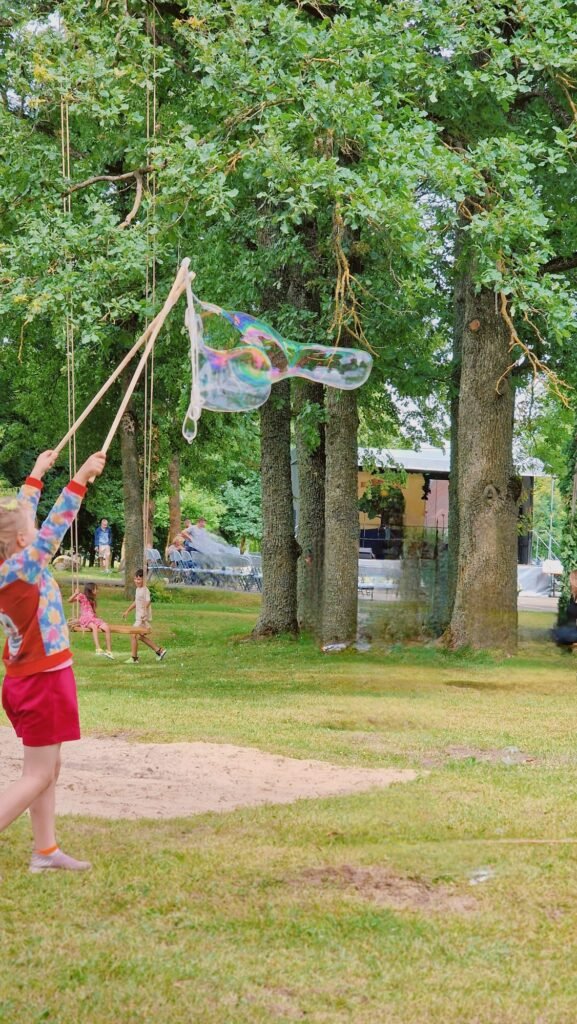 Medžio Karma muilo burbulų lazdelė – mergaitė lauke kuria burbulus su medinėmis lazdelėmis