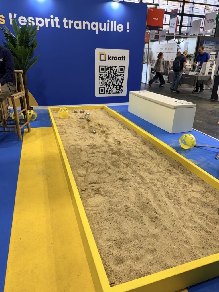 Petankės aikštelė su smėliu ir metaliniais rutuliais parodos stende Paris Builders Show – žaidimas lankytojams pritraukti